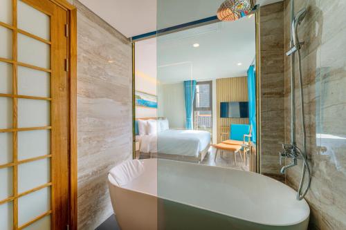 a bathroom with a bath tub and a bedroom at Sala Quy Nhon Beach Hotel in Quy Nhon
