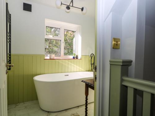 a bath tub in a green bathroom with a window at Hyrst Rise in Forest Row