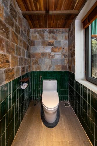 a bathroom with a toilet in a green tiled wall at Hang Mua Ecolodge in Ninh Binh
