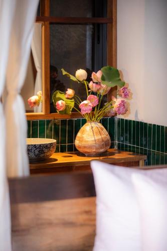 a vase with flowers on a table with a window at Hang Mua Ecolodge in Ninh Binh