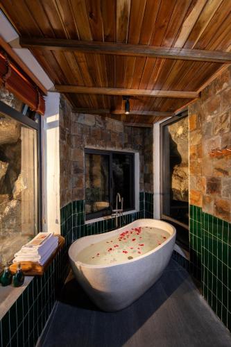 a bath tub in a bathroom with a stone wall at Hang Mua Ecolodge in Ninh Binh