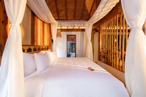 a bedroom with a white bed with white curtains at Hang Mua Ecolodge in Ninh Binh