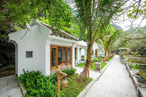 a white house with palm trees and a sidewalk at Hang Mua Ecolodge in Ninh Binh