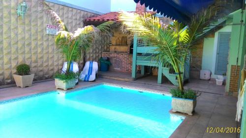 a swimming pool with palm trees next to a house at Suítes Casa Verde in Arraial do Cabo