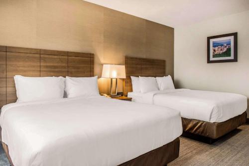 two beds in a hotel room with white sheets at Quality Hotel Dorval Aeroport in Dorval
