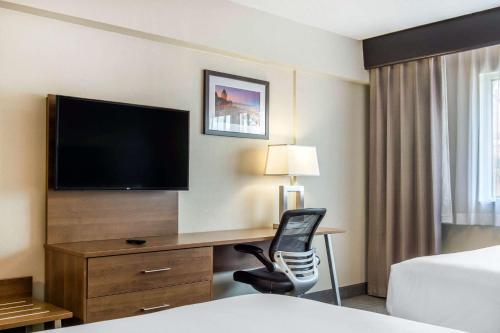 a hotel room with a bed and a desk with a television at Quality Hotel Dorval Aeroport in Dorval