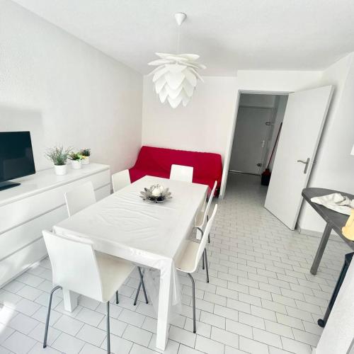 une salle à manger avec une table blanche et un canapé rouge dans l'établissement SECTEUR SEAQUARIUM - APPARTEMENT 6 PERS CLIMATISE RDC, 1 CHAMBRE - GRANDE TERRASSE, au Grau-du-Roi