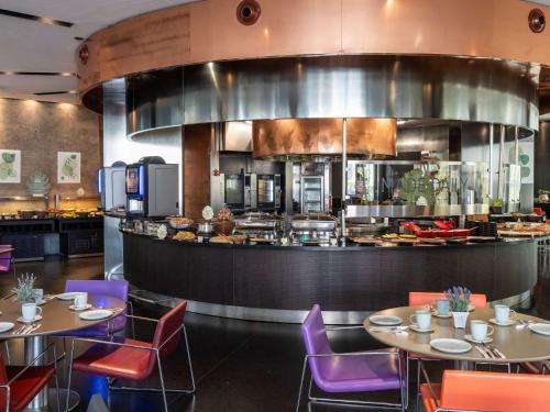 a restaurant with tables and chairs and a kitchen at Novotel Barcelona City in Barcelona