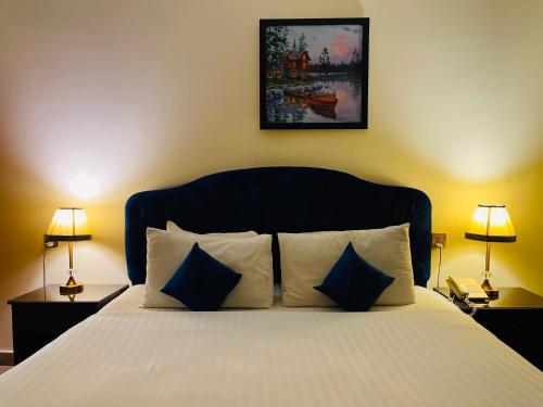a bedroom with a bed with blue pillows and two lamps at Infinity Hotel in Lahore