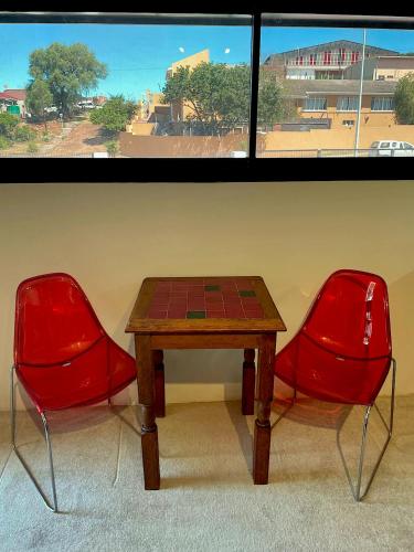 two red chairs and a wooden table in front of a window at Mount Road Suites in Port Elizabeth