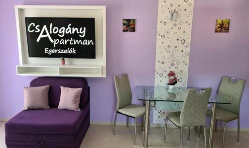 a dining room with a purple couch and a glass table at Csalogány Apartman Egerszalók in Egerszalók