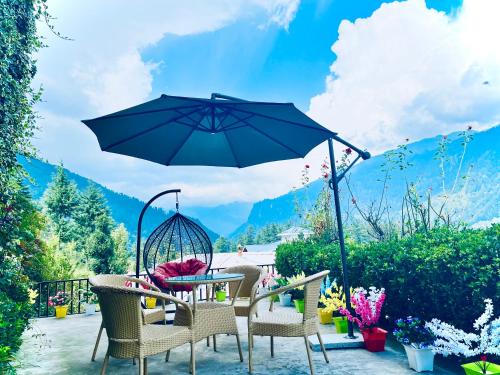 a patio with a table and chairs and an umbrella at 4 Bedroom Luxury Bungalow In Manali With Beautiful Scenic Mountain & Orchard View - #Private Bungalow #Premium Big rooms #Parking #Guest Preferred in Manāli