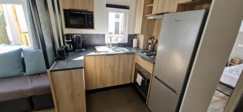 a small kitchen with a refrigerator and a sink at Cosy mobil home 3Ch en forêt, parking inclus, plage à 15mn à pied in Capbreton