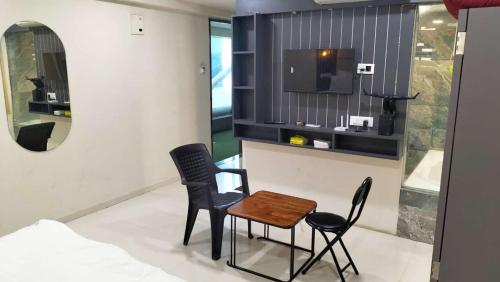 a room with two chairs and a table and a tv at hotel the crown in Surat