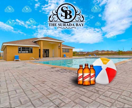 two bottles of beer and a beach umbrella next to a swimming pool at The Surada Bay 2 bedrooms in Old Harbour