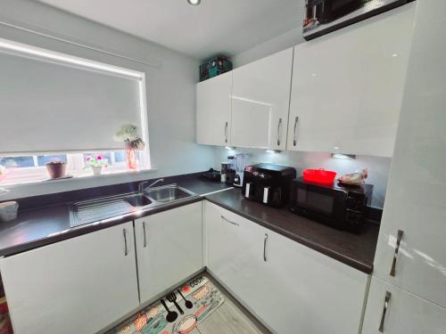 a kitchen with white cabinets and a sink and a microwave at Charming Room, shared house in Oldham