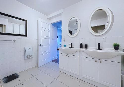 a white bathroom with two sinks and two mirrors at Élégant et cosy - 2 chambres bien équipé et parking gratuit in Montréal