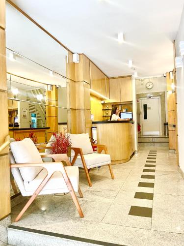 a living room with white chairs and a kitchen at Hotel BH Palace in Belo Horizonte