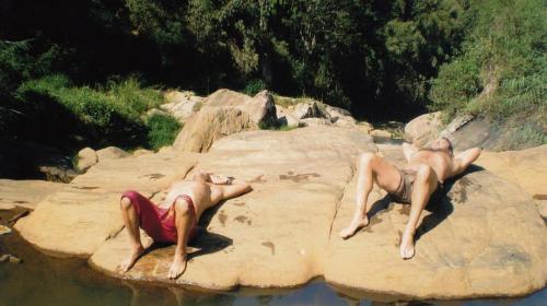 two men laying on a rock in the water at The River Hut Resort Hatton in Hatton
