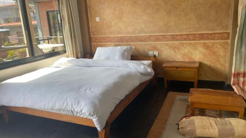 a bed with white sheets in a room with a window at Hotel Hakoniwa in Pokhara
