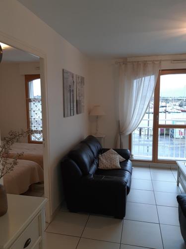 a living room with a black leather couch and a window at Résidence Les Pêcheries in Saint-Vaast-la-Hougue
