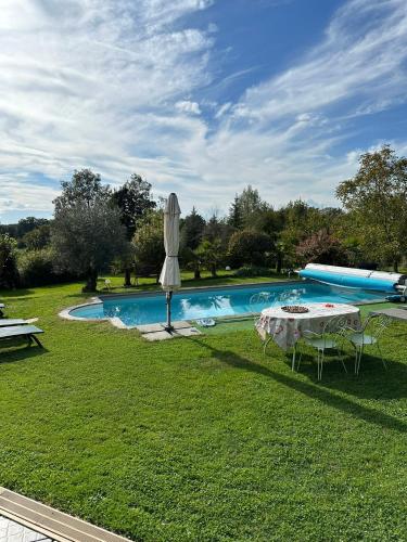 une piscine avec une table et un parasol dans l'herbe dans l'établissement La Ferme de Jad, à Louhans