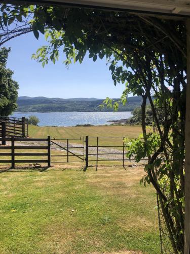 a fence with a view of a field and a lake at Ellary Cottage in Lochgilphead