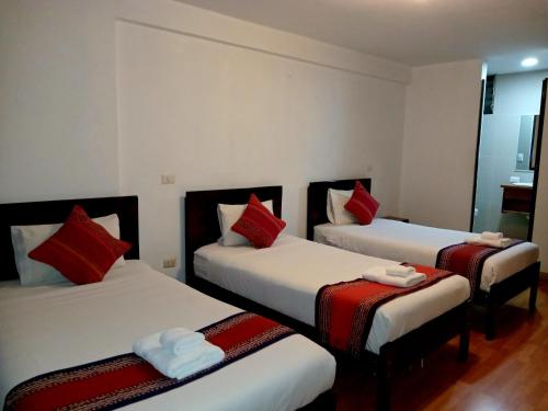 a room with three beds with red pillows at El Quetzal MachuPicchu in Machu Picchu