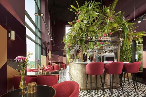 a restaurant with red chairs and a bar with plants at The Den, 's-Hertogenbosch, a Tribute Portfolio Hotel in Den Bosch