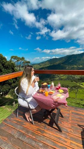 a woman sitting at a picnic table with a glass of wine at Cabanas Bela Vista in São Bento do Sapucaí