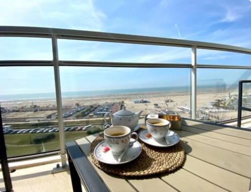 deux tasses de café sur une table sur un balcon dans l'établissement Le Front de mer - Centre-ville - Vue mer - Parking gratuit, à Le Touquet-Paris-Plage