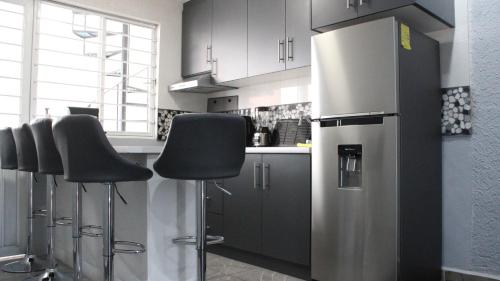 a kitchen with a stainless steel refrigerator and bar stools at Comodo apartamento de 3 habitaciones, a 10 min en vehiculo del Zocalo de Oaxaca in Oaxaca City