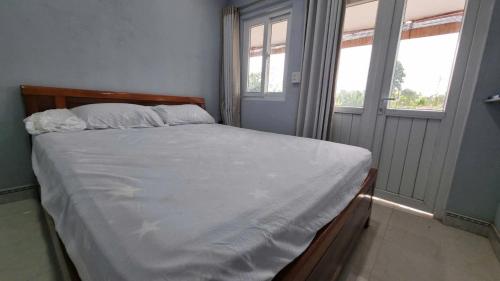 a bedroom with a bed with white sheets and two windows at YÊN Homestay in Dien Ban