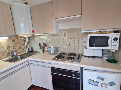 La cuisine est équipée de placards blancs, d'un four micro-ondes et d'une cuisinière. dans l'établissement Studio climatisé près de la plage et commerces, parking, animaux acceptés, Sainte-Maxime - FR-1-780-92, à Sainte-Maxime