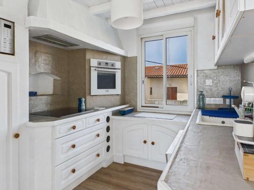 une cuisine avec des placards blancs et une grande fenêtre dans l'établissement Maison 8 pers Front de Mer - Grau d'Agde - FR-1-423-320, au Grau-dʼAgde