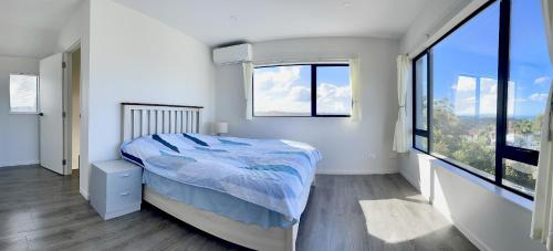 a white bedroom with a bed and large windows at Valley Sea View Villa Torbay in Auckland