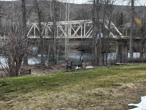 a park bench next to a river with a bridge at Methow River Lodge and Cabins in Winthrop
