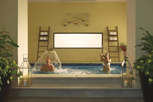 Dos personas en una piscina con pantalla blanca en Dreams Los Cabos Suites Golf Resort & Spa, en Cabo San Lucas