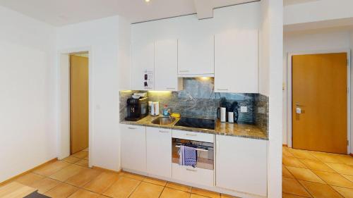 a kitchen with white cabinets and a wooden floor at Zentral Altstadt Chur - Bahnhofsnah - Ferienwohnung - Bernina Express - Solution-Grischun in Chur