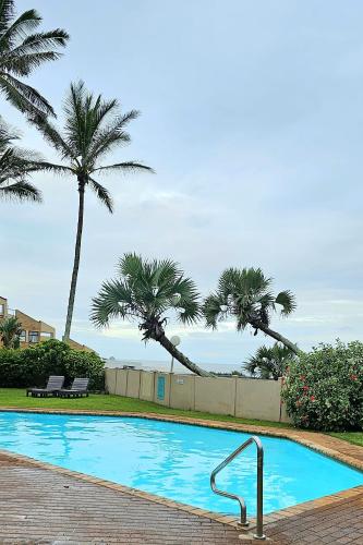 a swimming pool with palm trees in the background at 10 Coral Cove Beach Lodge in Ballito