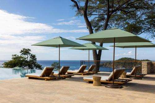 a group of lounge chairs and umbrellas next to the water at Nekajui, a Ritz-Carlton Reserve in Papagayo, Guanacaste