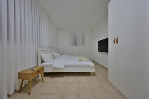 a white bedroom with a bed and a table at פנטהאוז 125 - פנטהאוז, דירת אירוח וגג מהמם לאירועים עם בריכה וגקוזי in Nahariyya