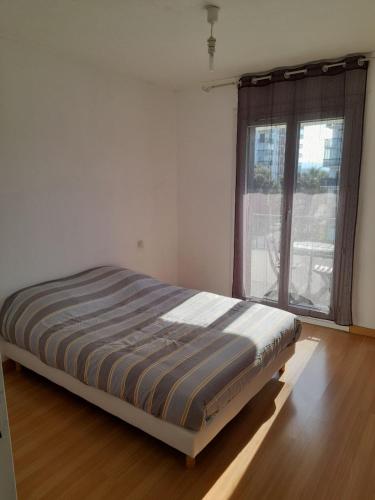 un lit dans une chambre avec une grande fenêtre dans l'établissement Bel appartement Perpignan 15 min de la mer, à Perpignan