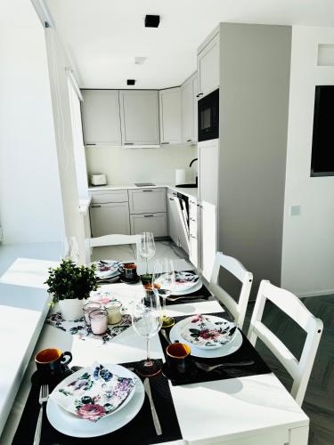 a kitchen with a table with plates and wine glasses at White Apartment in Liepāja