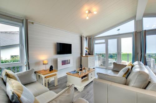 Una sala de estar con muebles blancos y grandes ventanales. en Gimblet Rock Holiday Park, en Pwllheli