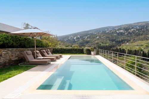 a swimming pool with chairs and an umbrella at SuiteHome Villas with Private Pools by Explore Andros in Andros