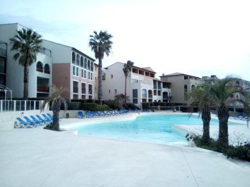 - une piscine avec des chaises bleues et des palmiers dans l'établissement Duplex vue mer- Six-fours-les-plages, à Six-Fours-les-Plages
