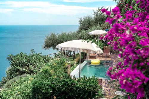 a swimming pool with two umbrellas and purple flowers at Villa San Cosma in Ravello