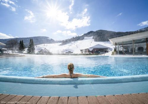 a woman laying in a swimming pool in the snow at Chalet Bergblick Suites - Luxury Escape in Bad Kleinkirchheim