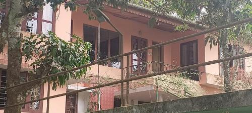 a pink building with a balcony and a tree at East West Farm Homestay in Munnar